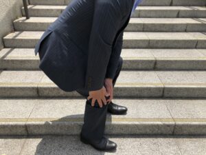 石段で膝を押さえるスーツ姿の人